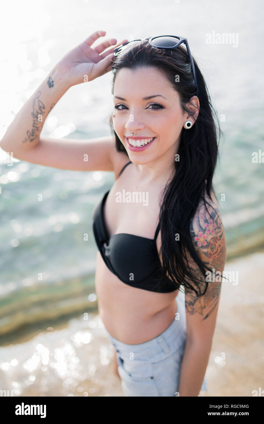 Ritratto di sorridente giovane donna con naso piercing e tatuaggio permanente al mare Foto Stock