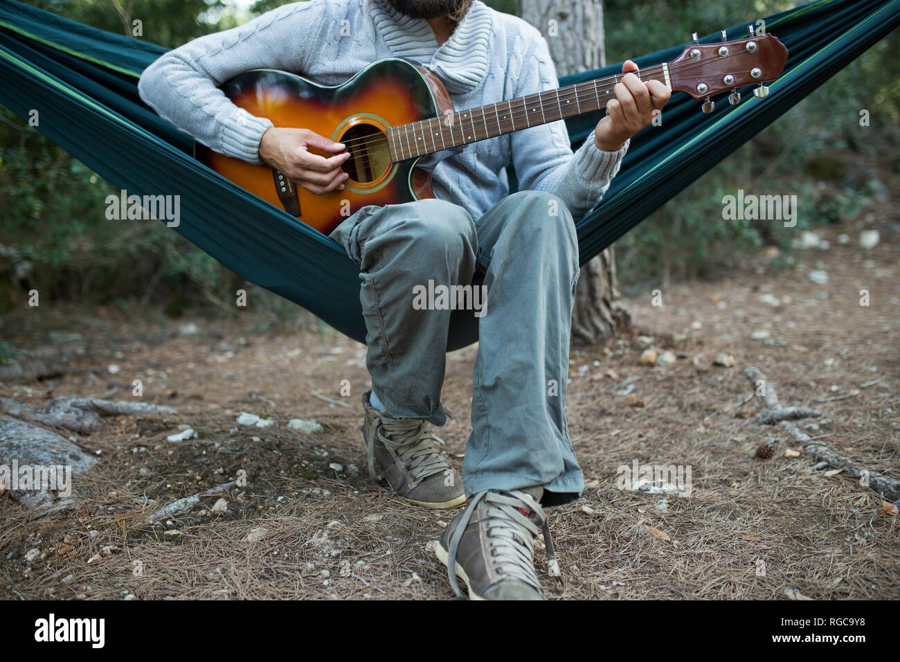 Uomo seduto in amaca a suonare la chitarra nei boschi, vista parziale Foto Stock