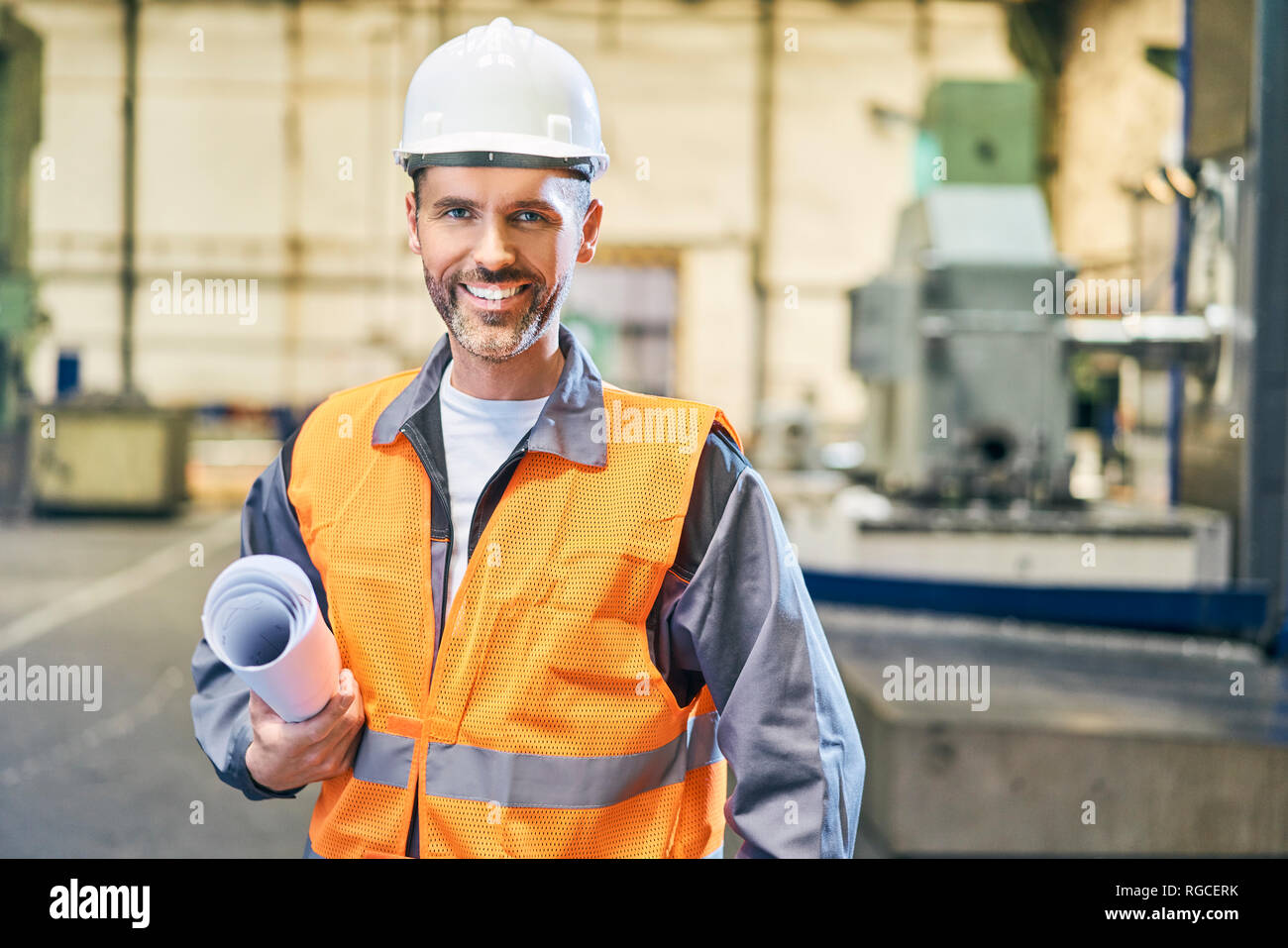 Ritratto di uomo sorridente holding blueprint in fabbrica Foto Stock