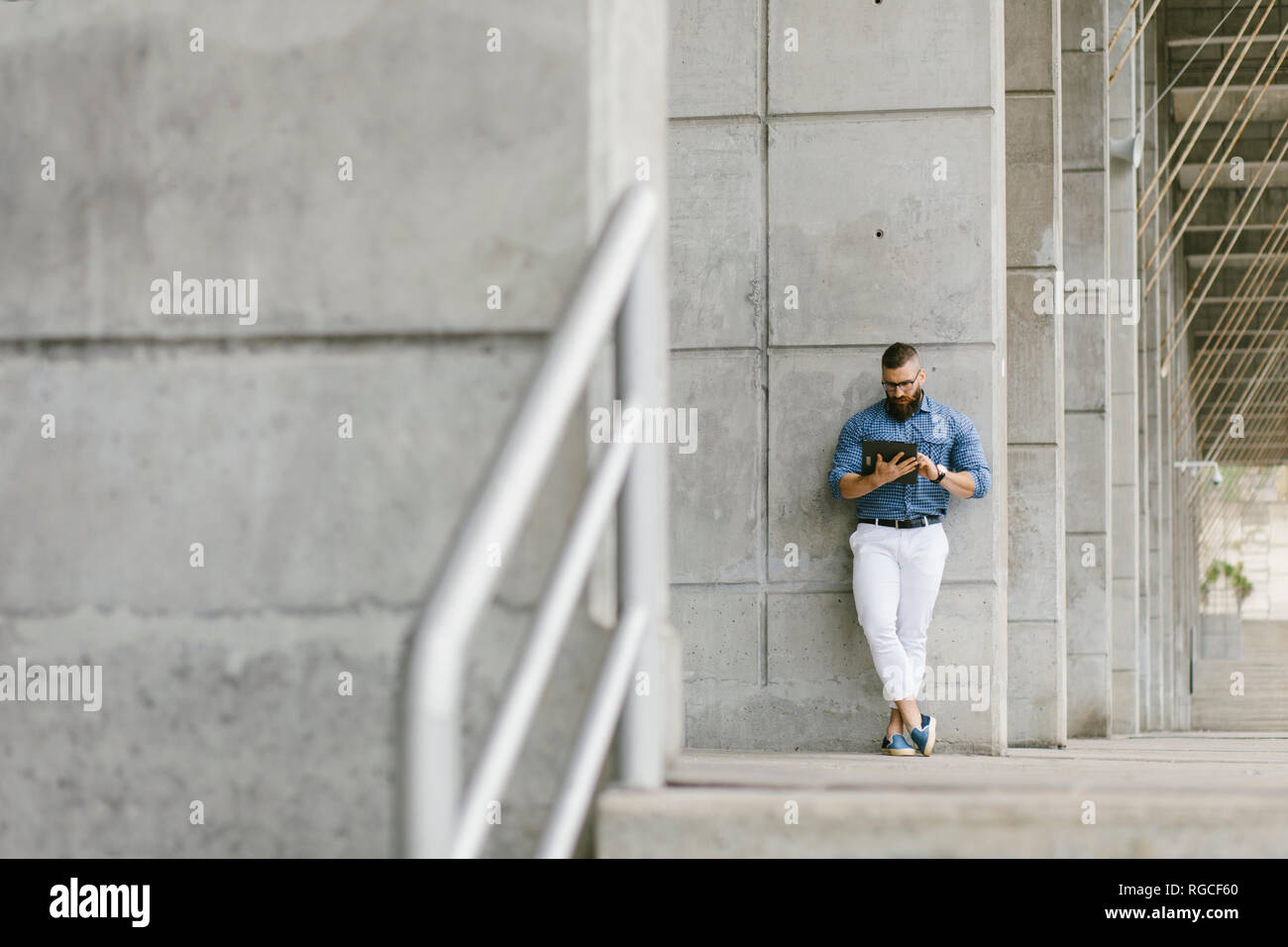 Tanga barbuto imprenditore appoggiata contro la parete di cemento utilizzando tablet Foto Stock