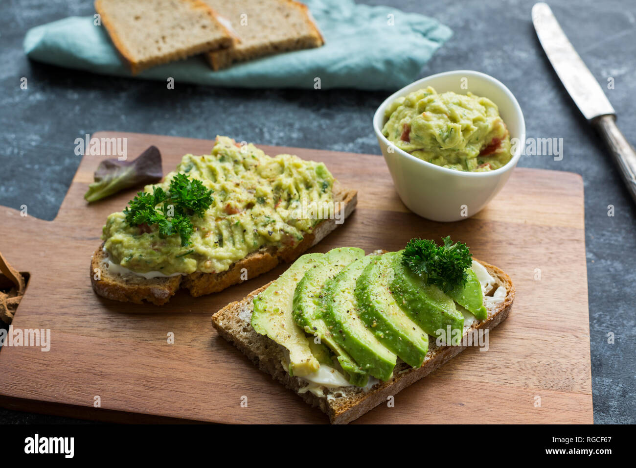 Fette di pane con fette di avocado e crema di avocado su pannello di legno Foto Stock