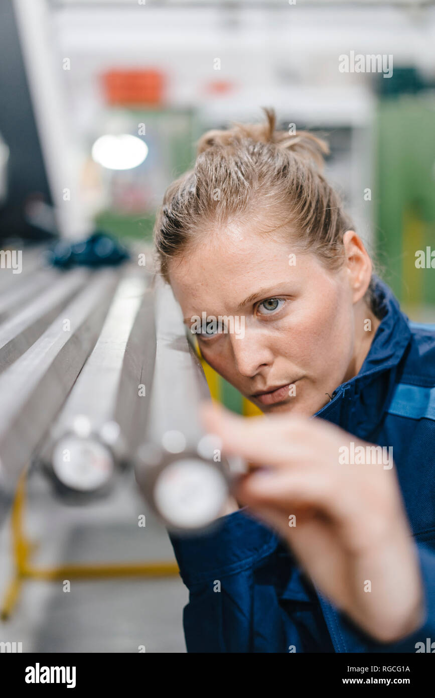 Giovane donna che lavora come un operaio specializzato in un high tech company, controllo aste in acciaio Foto Stock
