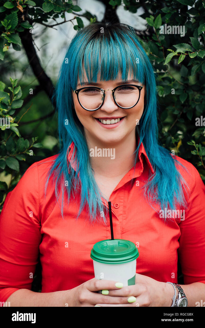 Ritratto di sorridente giovane donna con tinti di blu capelli e bevanda Foto Stock