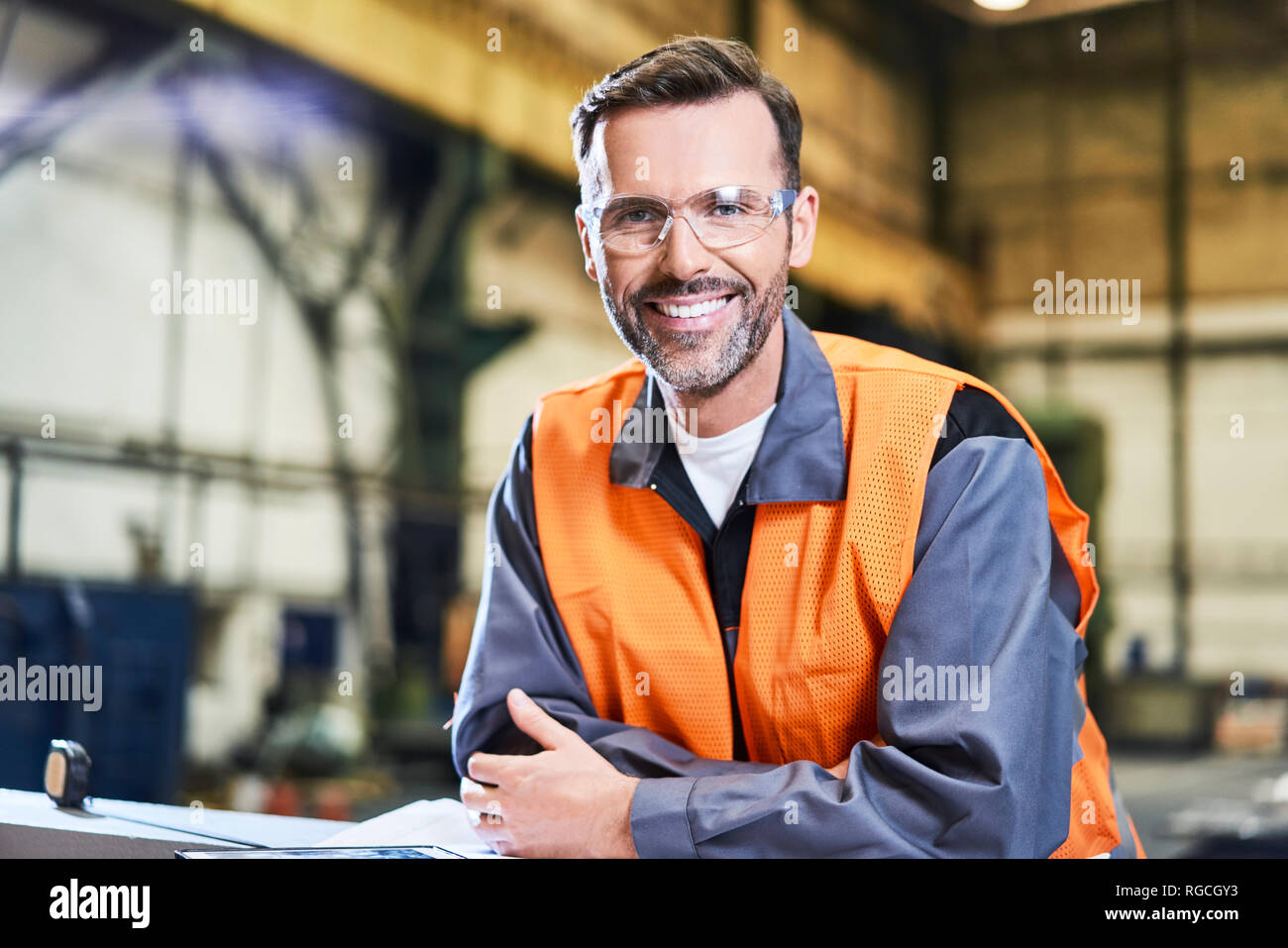 Ritratto di uomo sorridente in fabbrica che indossa gli occhiali di protezione Foto Stock