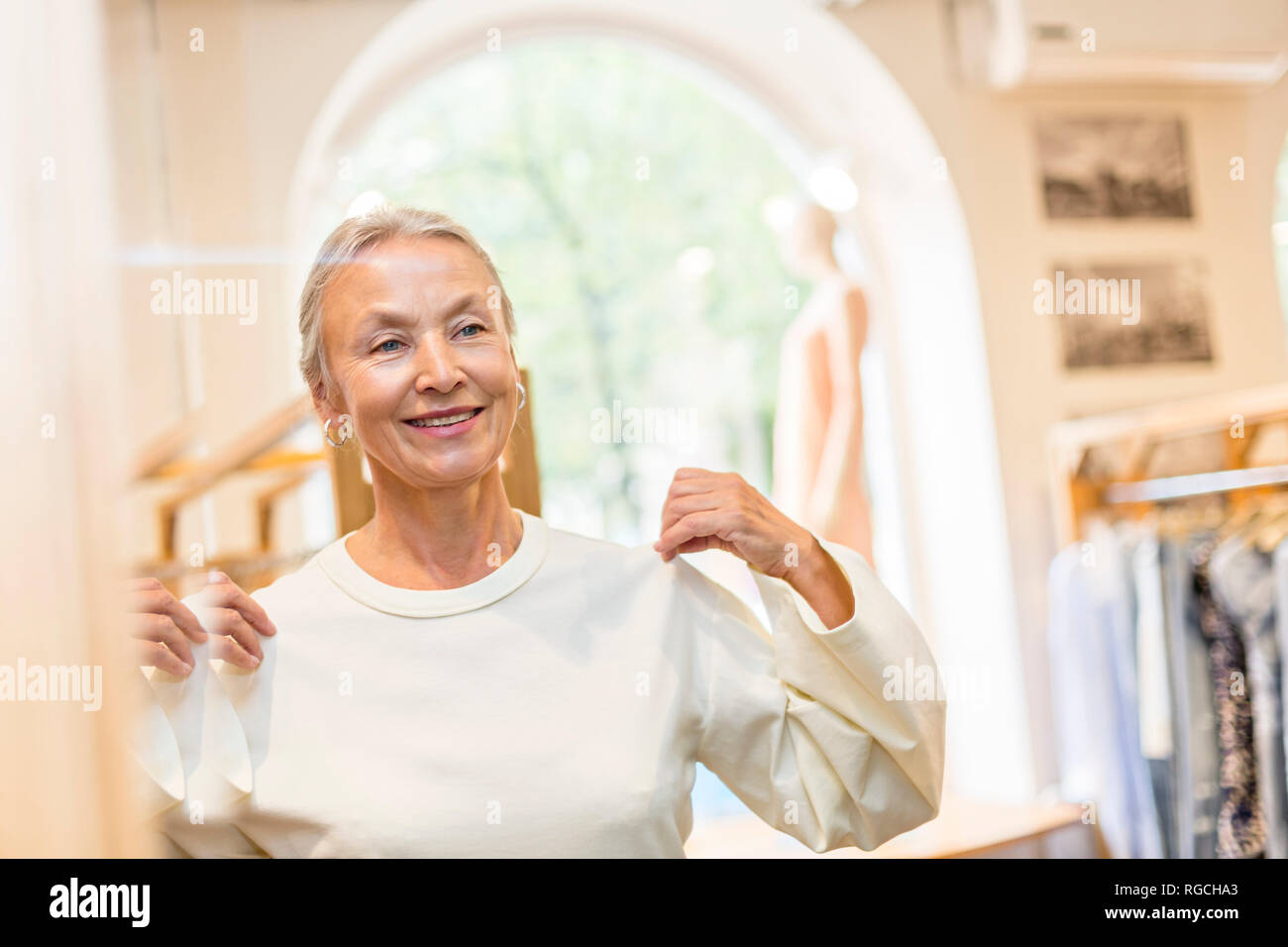 Sorridente donna senior cercando su pullover in un boutique hotel Foto Stock