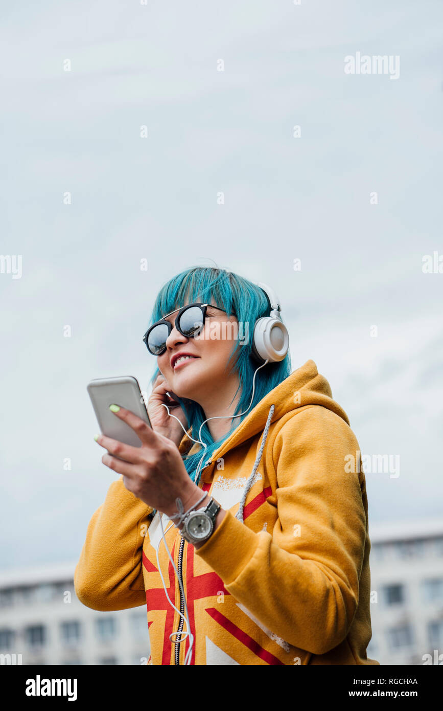 Ritratto di giovane donna con tinti di blu capelli ascoltando musica con lo smartphone e le cuffie Foto Stock