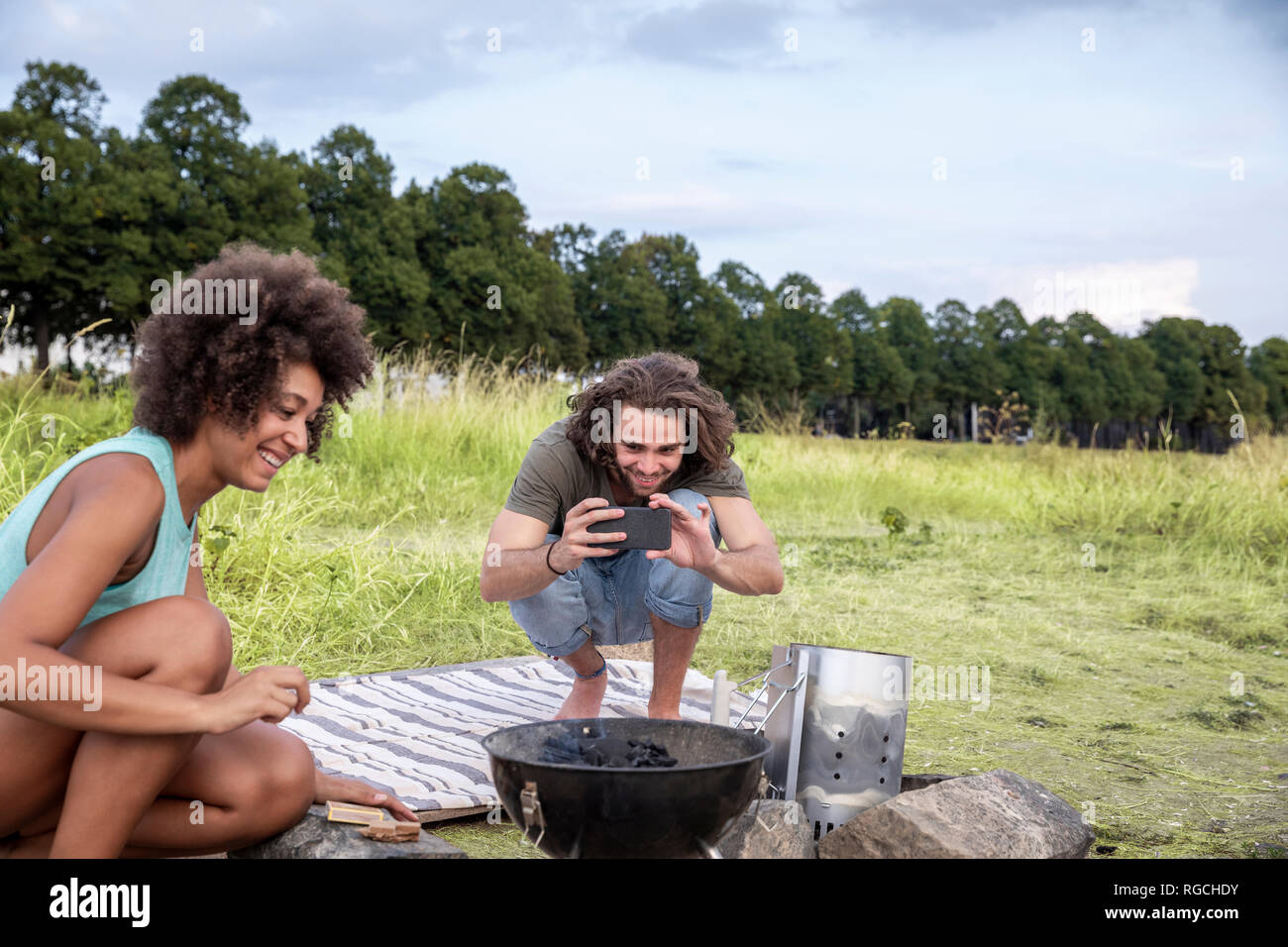 Sorridente giovane uomo con la fidanzata di scattare una foto di un barbecue nella natura Foto Stock