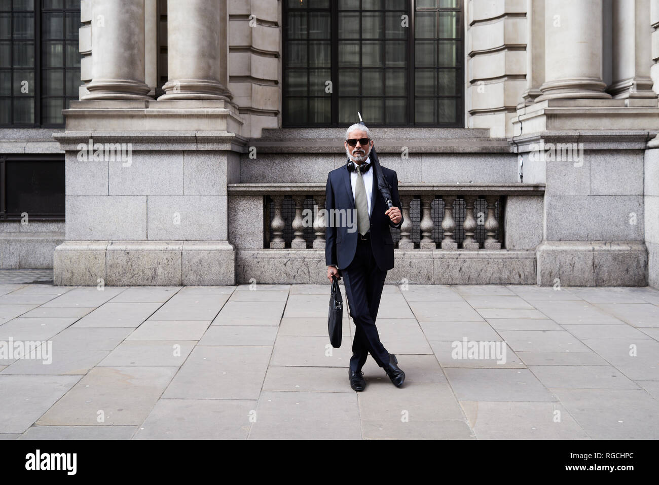 UK, Londra, ritratto di elegante imprenditore con occhiali da sole e ombrello indossare tuta e tirante Foto Stock