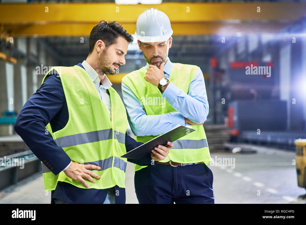 Due gestori di indossare indumenti da lavoro protettiva guardando negli appunti in fabbrica Foto Stock