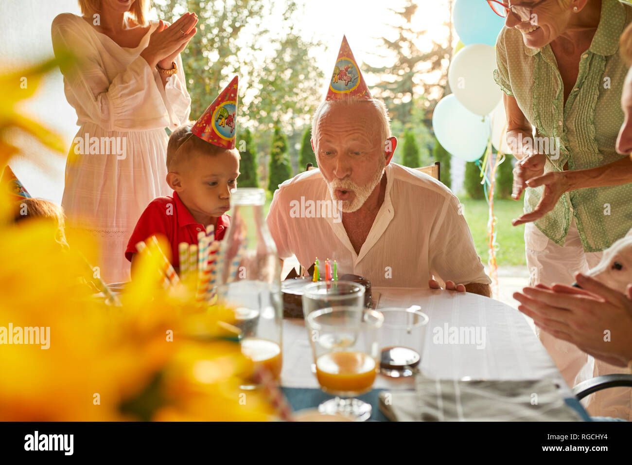 Felice famiglia estesa soffiando le candeline sulla torta di compleanno in un party in giardino Foto Stock