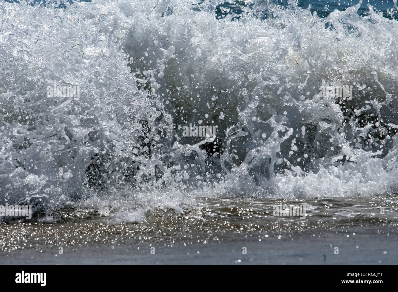 Un'onda si blocca sulla battigia thosing goccioline di acqua in ogni direzione. Foto Stock