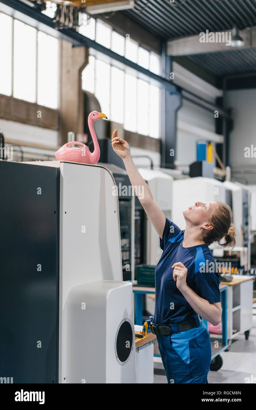 Giovane donna che lavora come un operaio specializzato in un high tech company, giocando con un fenicottero rosa Foto Stock
