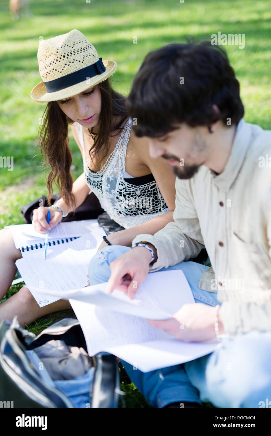 Due studenti seduti su un prato in un parco guardando le note Foto Stock