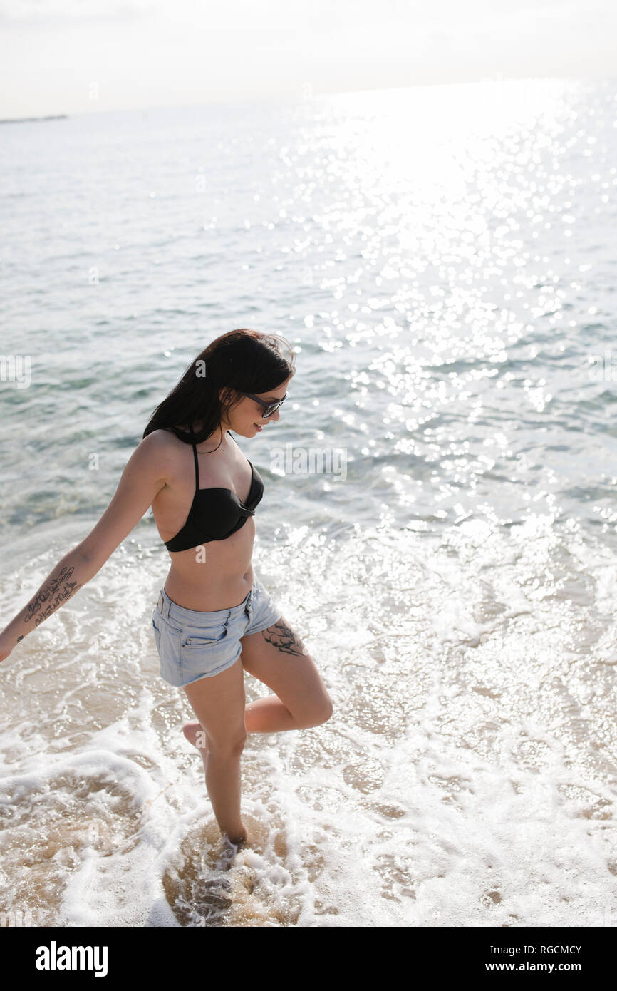 Sorridente giovane donna con tatuaggi wading al mare Foto Stock