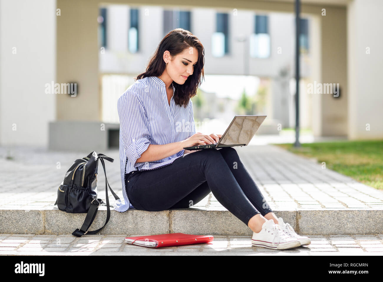 Contenuto studente seduto sul gradino esterno lavorando sul computer portatile Foto Stock