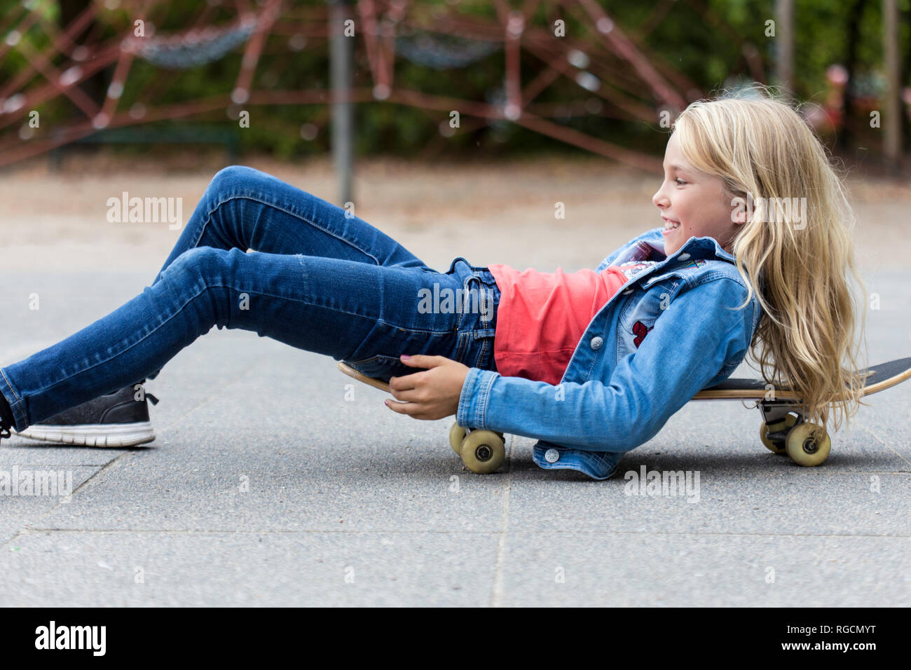 Sorridente ragazza bionda con lo skateboard su parco giochi Foto Stock