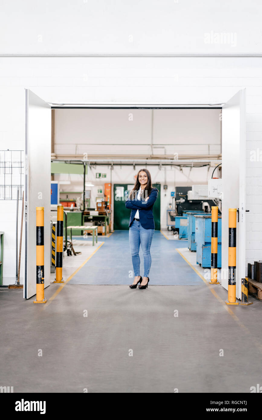 Fiducioso donna che lavorano in high tech enterprise, stando in officina in fabbrica con le braccia incrociate Foto Stock