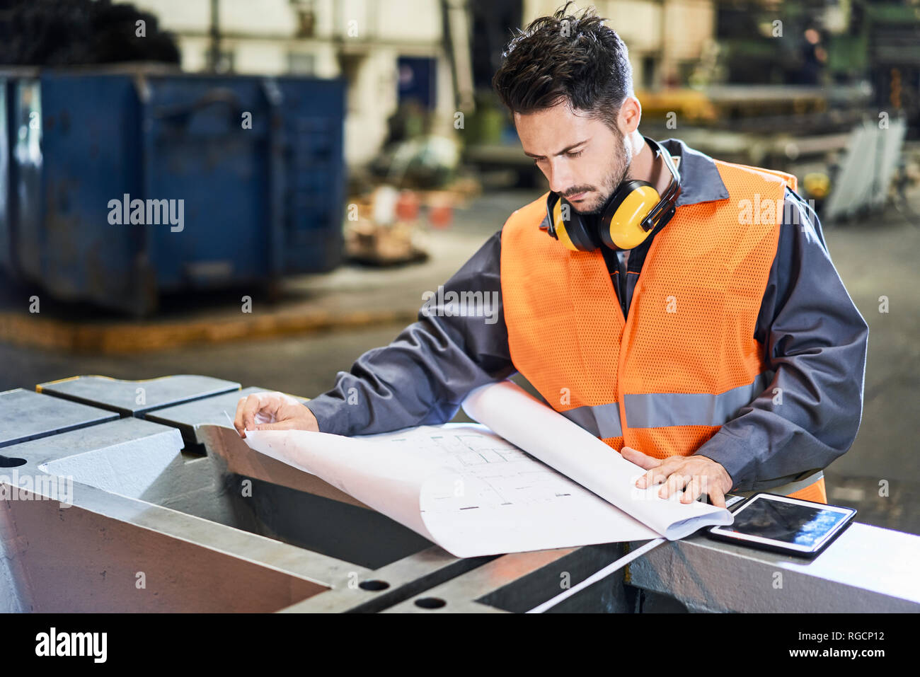 Uomo che indossa indumenti da lavoro protettiva guardando blueprint in fabbrica Foto Stock