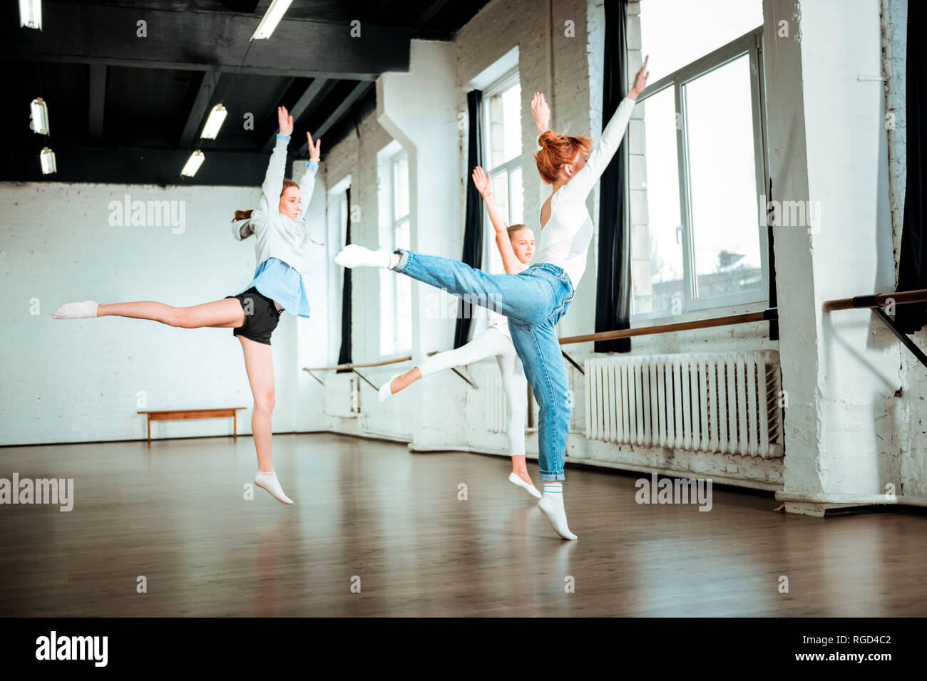 I capelli rossi insegnante di danza in jeans blu e i suoi studenti facendo oscillare la gamba Foto Stock