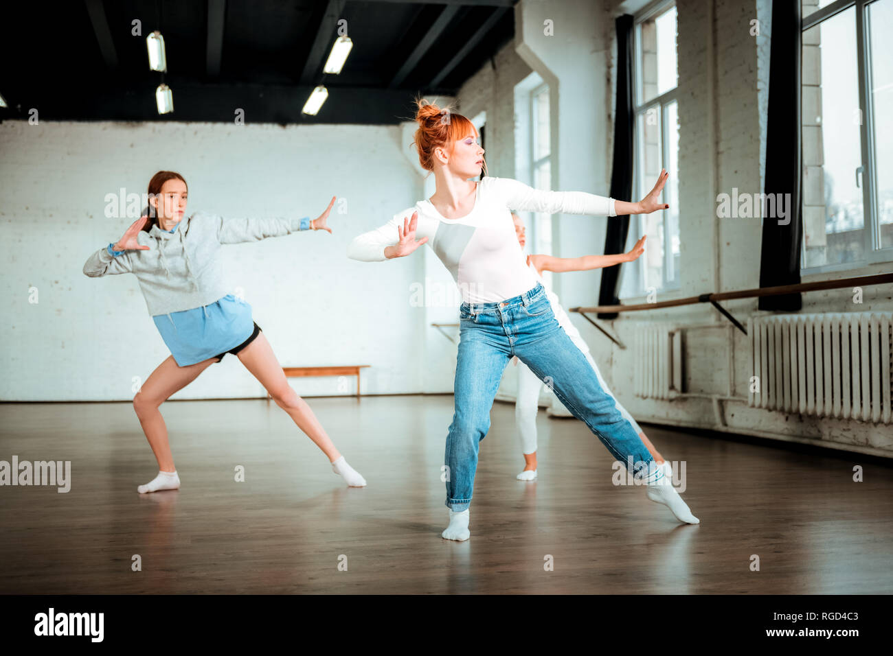 I capelli rossi insegnante di danza in jeans blu e i suoi studenti dancing attivamente Foto Stock