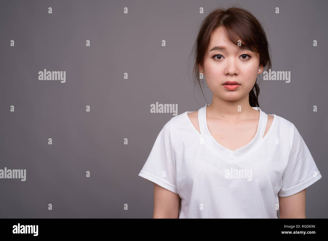 Giovane bella donna asiatica contro uno sfondo grigio Foto Stock