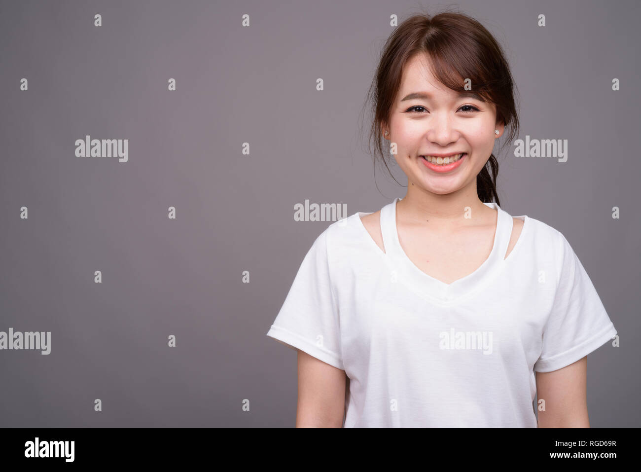 Felice donna asiatica sorridente contro uno sfondo grigio Foto Stock