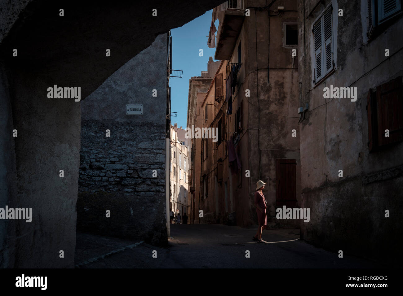 La Corsica, donna in piedi nella luce del sole, vicolo Foto Stock