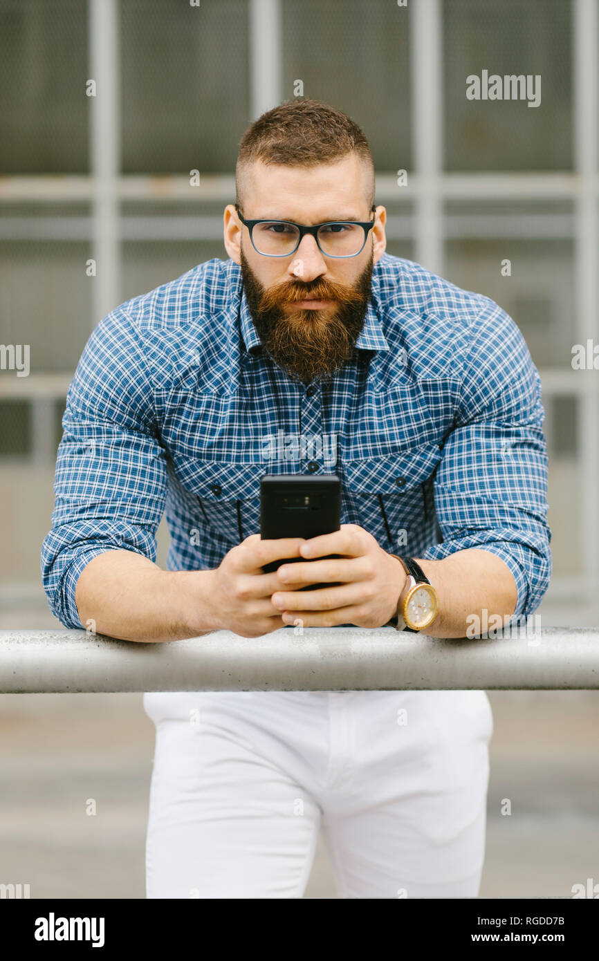 Ritratto di barbuto hipster imprenditore con inclinazione dello smartphone su parapetto Foto Stock