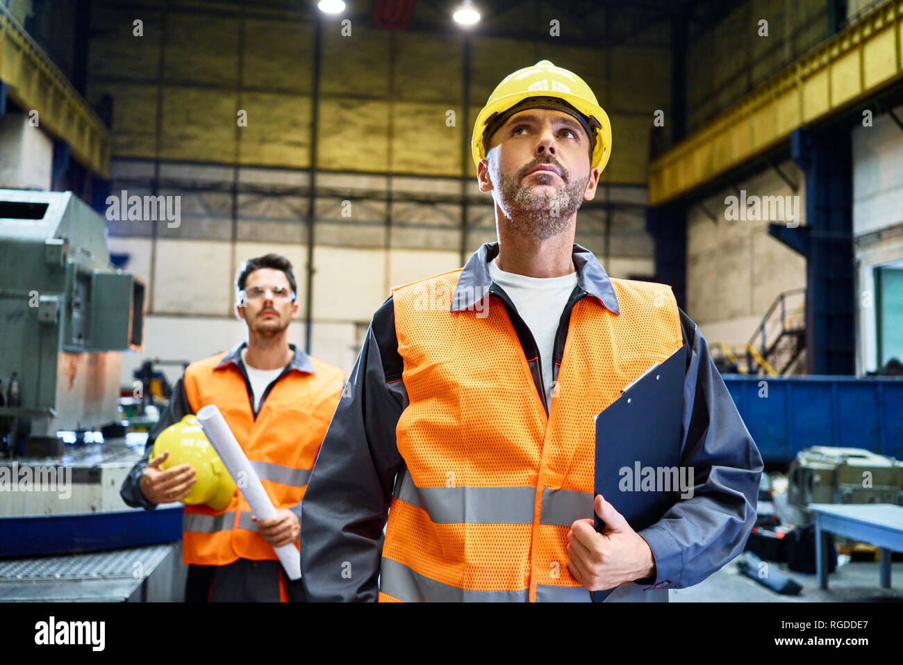 Due uomini che indossano indumenti da lavoro protettiva guardando intorno in fabbrica Foto Stock