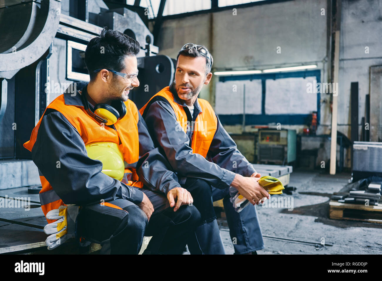 Due uomini che indossano indumenti da lavoro protettiva di parlare durante la pausa in fabbrica Foto Stock