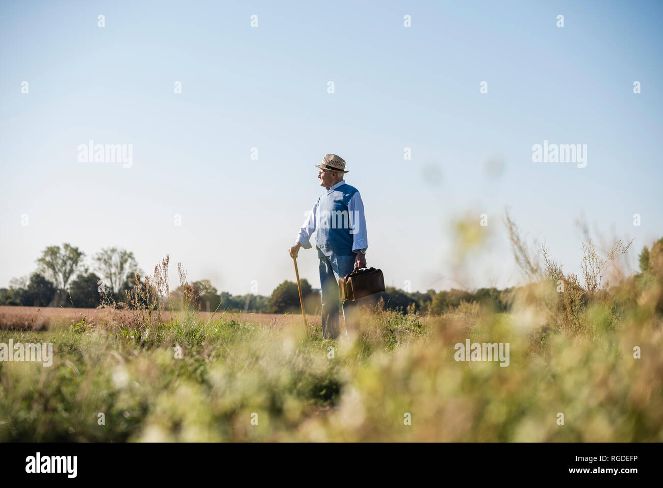 Senior uomo che porta borsa da viaggio, passeggiate nei campi Foto Stock