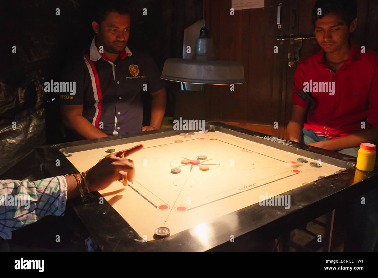 Tre uomini in uno squallido, cortile scuro 'club' in Mumbai, India, riproduzione del popolare gioco da tavolo Carrom (carambola) Foto Stock