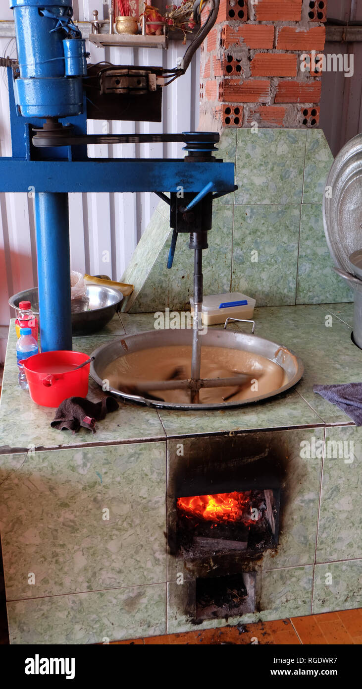Una macchina semplice agitazione sciolto lo zucchero di cocco per fare caramelle, con fuoco di seguito. Foto Stock