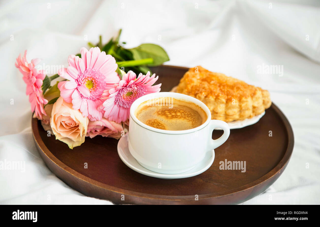 Bouquet di fiori con tazza di caffè e pasticceria bun sul vassoio in legno nel letto, mattina bed breakfast, romantico letto lo stile di vita di caffè Foto Stock