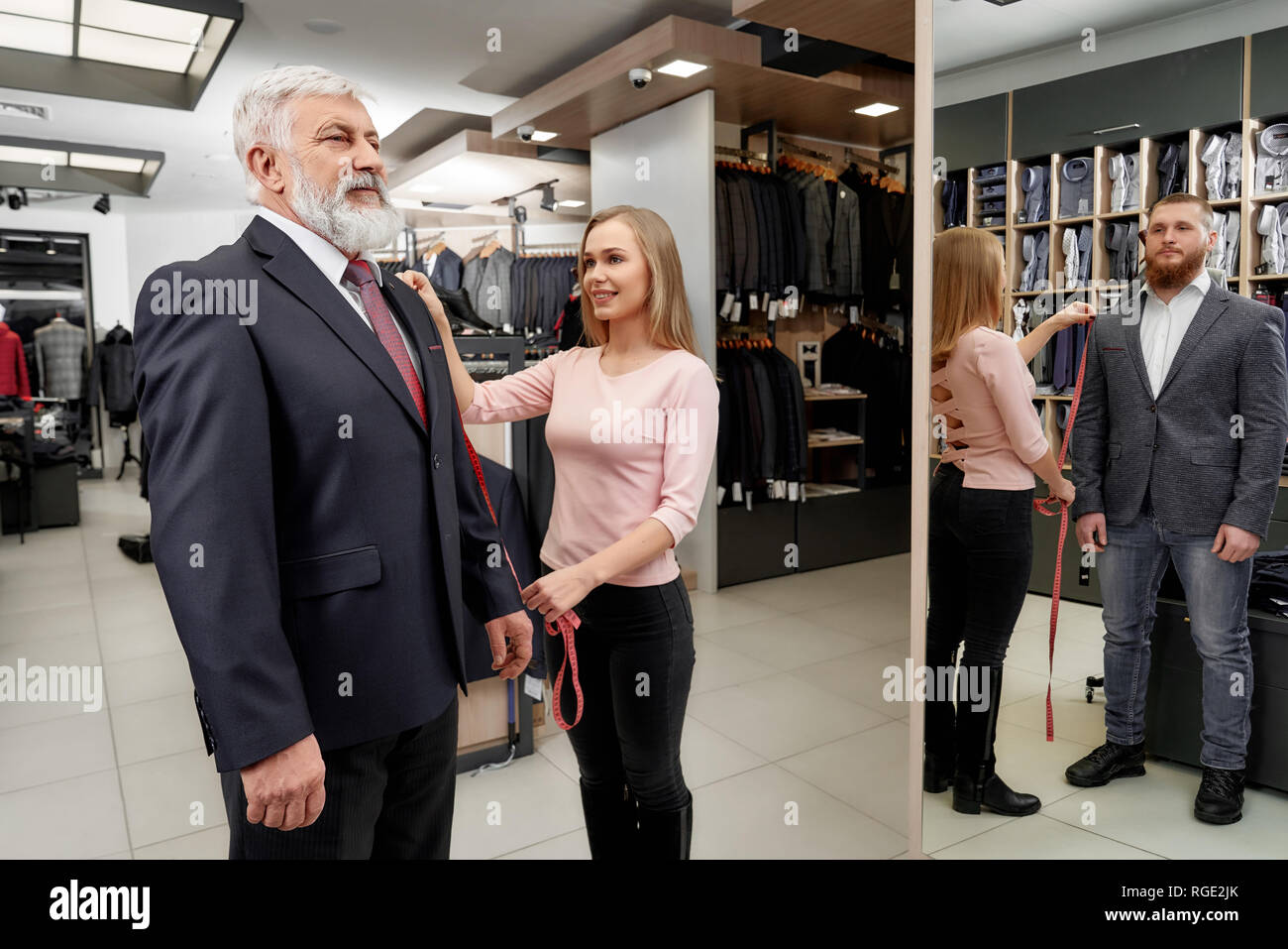 La Boutique con menswear. Uomo anziano cercando sul classico abito in  costoso negozio di abbigliamento. La riflessione a specchio del giovane  affascinante uomo che indossa in capi di abbigliamento alla moda. Assistant