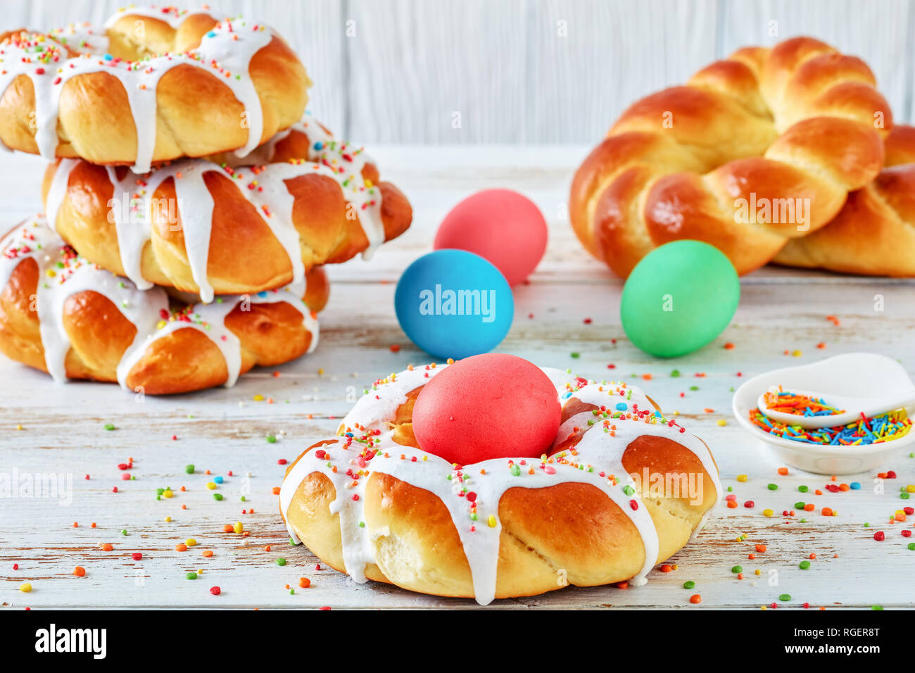Close-up di singoli dolci italiani intrecciato pane di Pasqua anelli intorno a vetri tinti uovo e guarnita con colorati spruzza su una rastrelliera, su un vecchio wh Foto Stock