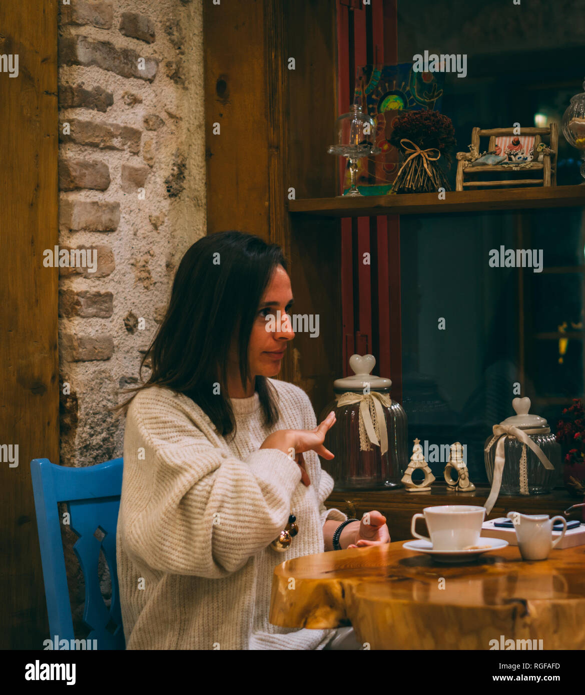 Giovane donna seduta nella caffetteria e parlare con il linguaggio dei segni. Esprimendo "oggi". Foto Stock