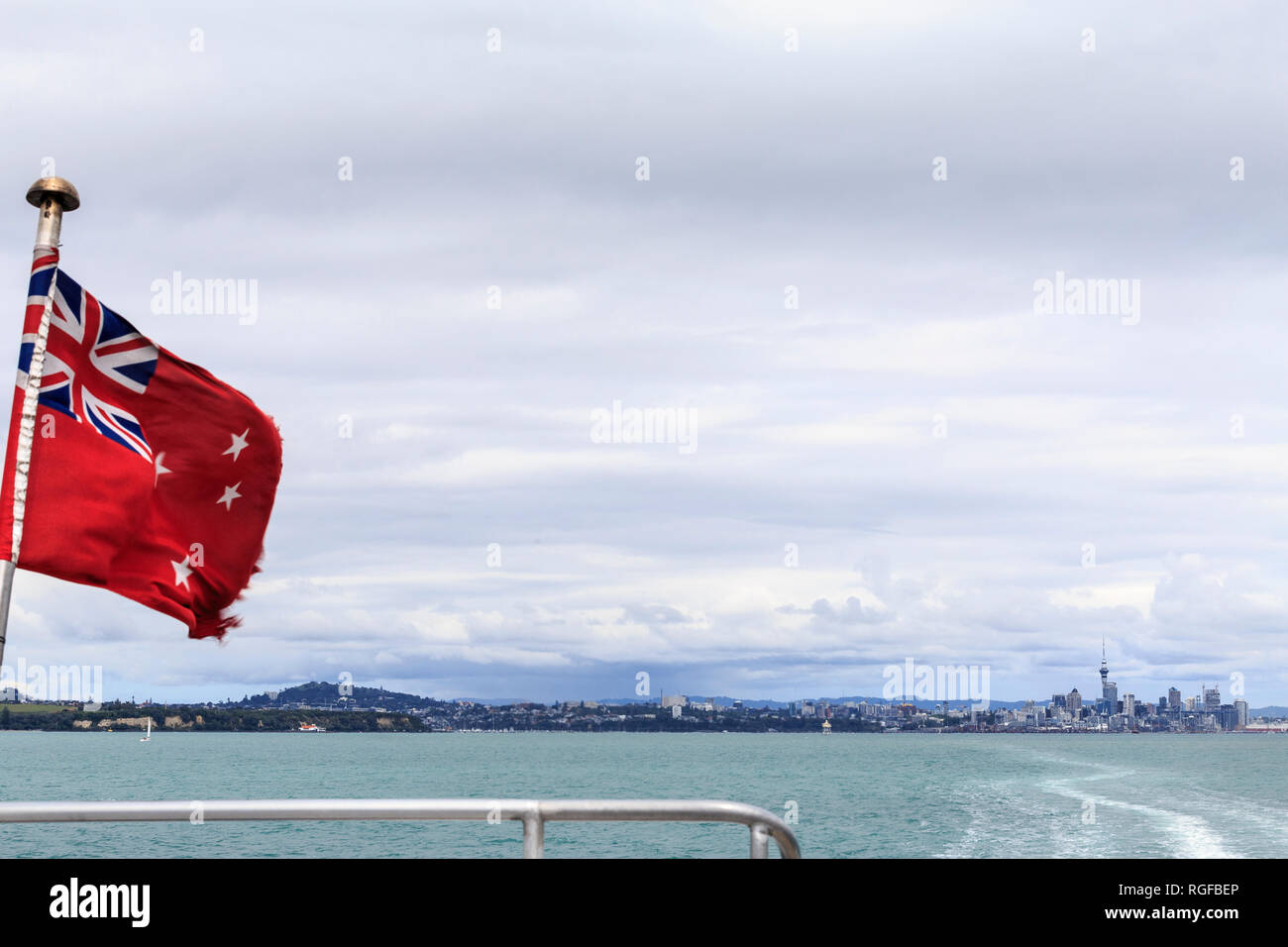 Leggermente strappati bandiera della Nuova Zelanda sul traghetto in uscita sul porto di Auckland, con rampa in barca e sveglia in acqua che porta indietro alla città di Auckland, inclu Foto Stock