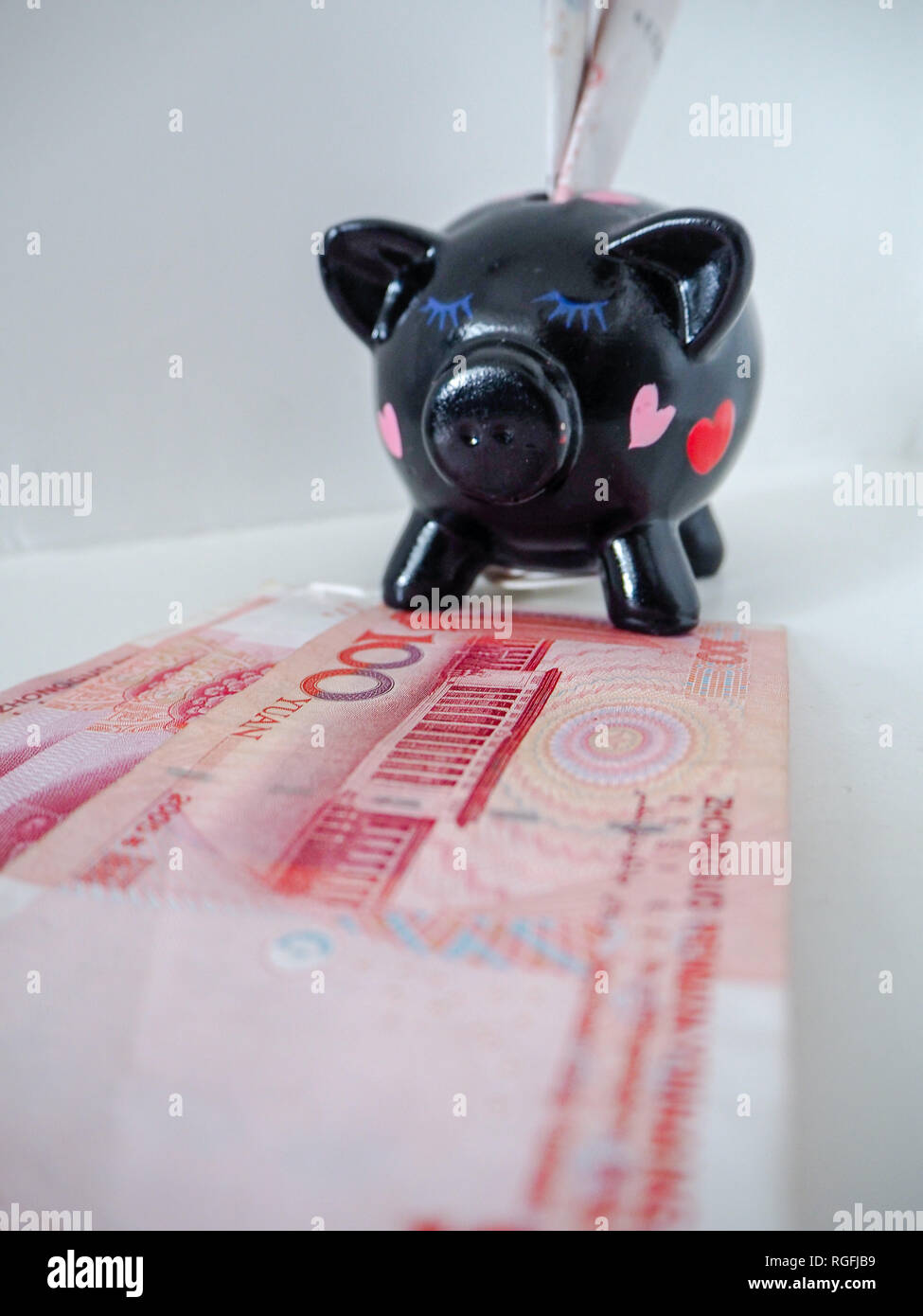 Nero salvadanaio in piedi accanto alla cinese 100 RMB banconote su un bianco sullo sfondo di legno. I simboli di maiale fortuna in zodiaco cinese. Foto Stock