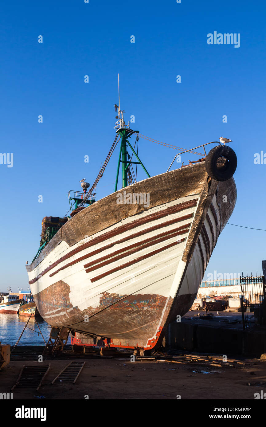 In legno barca di pesca al di fuori dell'Oceano Atlantico acqua, parcheggiato sulla riva. Bue luminoso cielo mattutino. Il vecchio porto originale a Essaouira, Marocco. Foto Stock