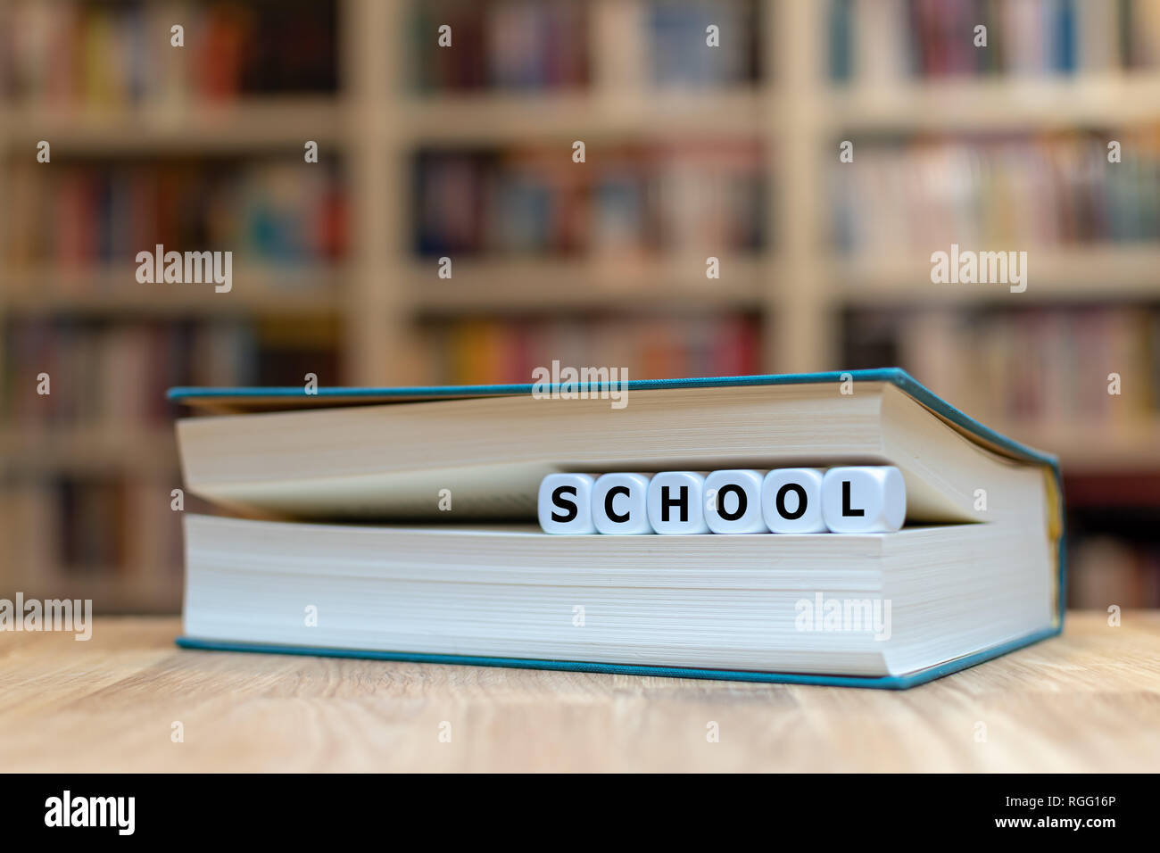 Dadi in una forma del libro la parola 'scuola'. Il libro è sdraiato su una scrivania di legno in una libreria. Foto Stock