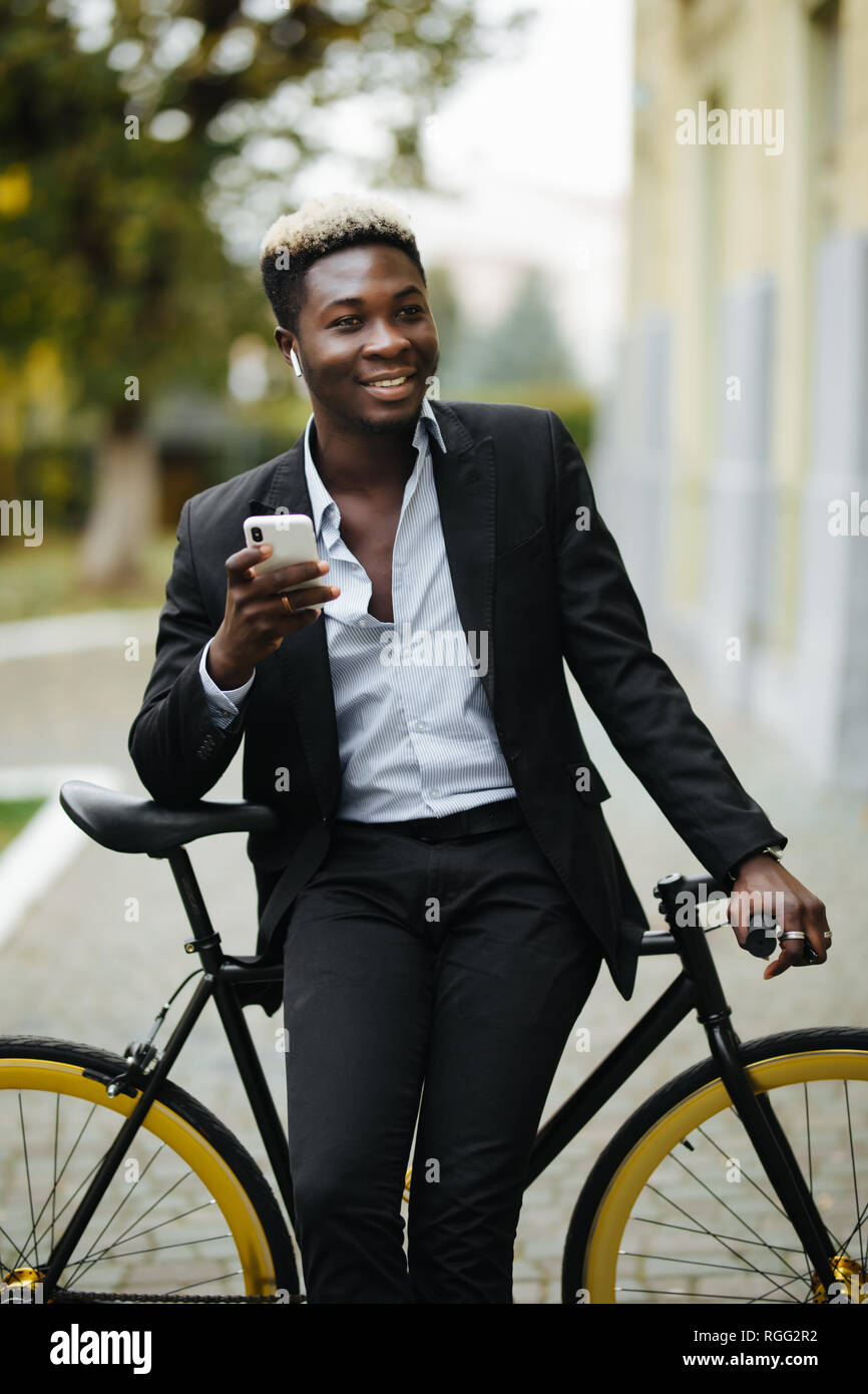 Sorridente giovane africano all'aperto, in piedi con la bicicletta,  l'ascolto di musica con le cuffie Foto stock - Alamy