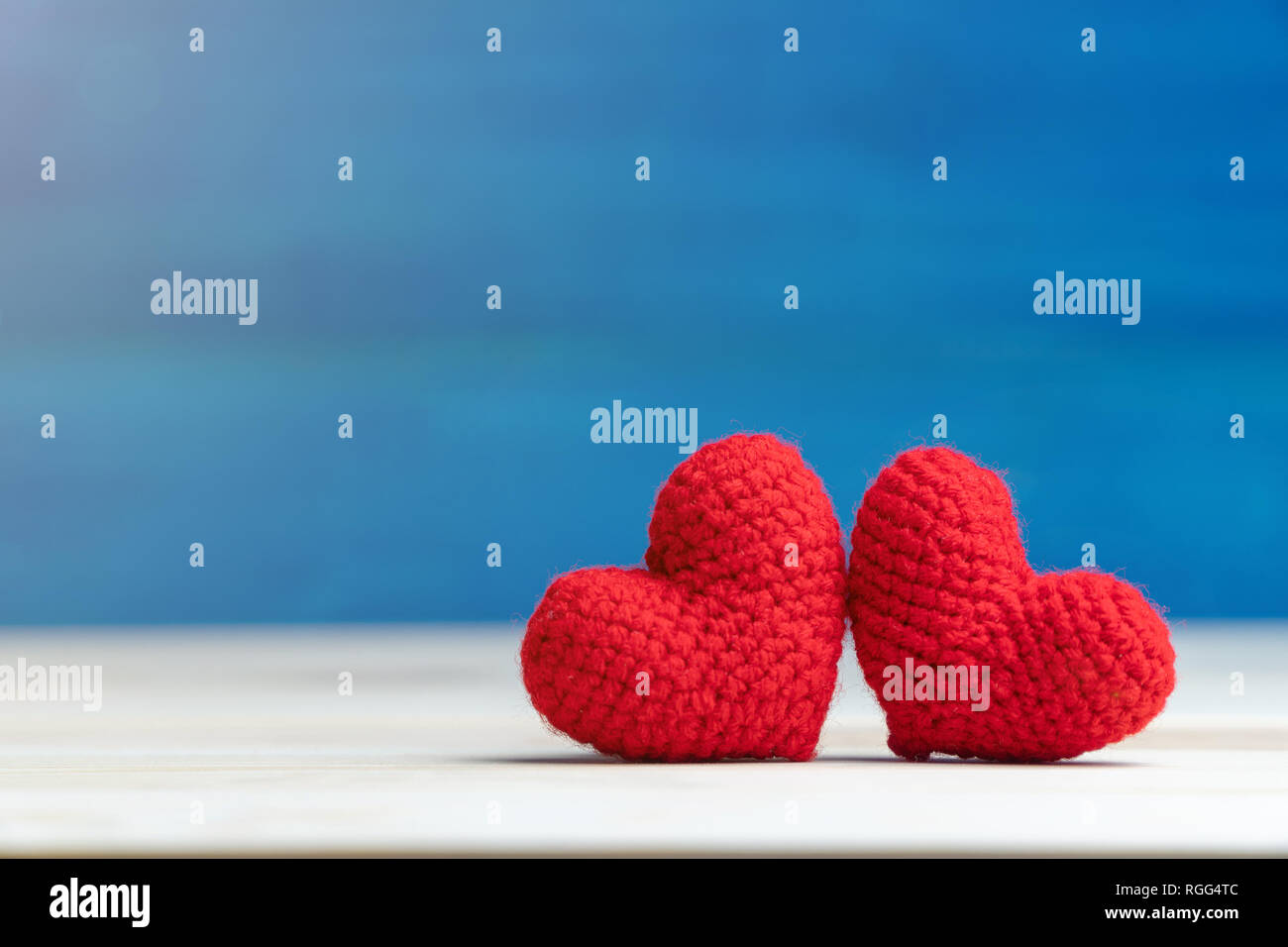 Il giorno di San Valentino concetto. mano fare due filati cuore rosso sul tavolo di legno e sfondo blu Foto Stock