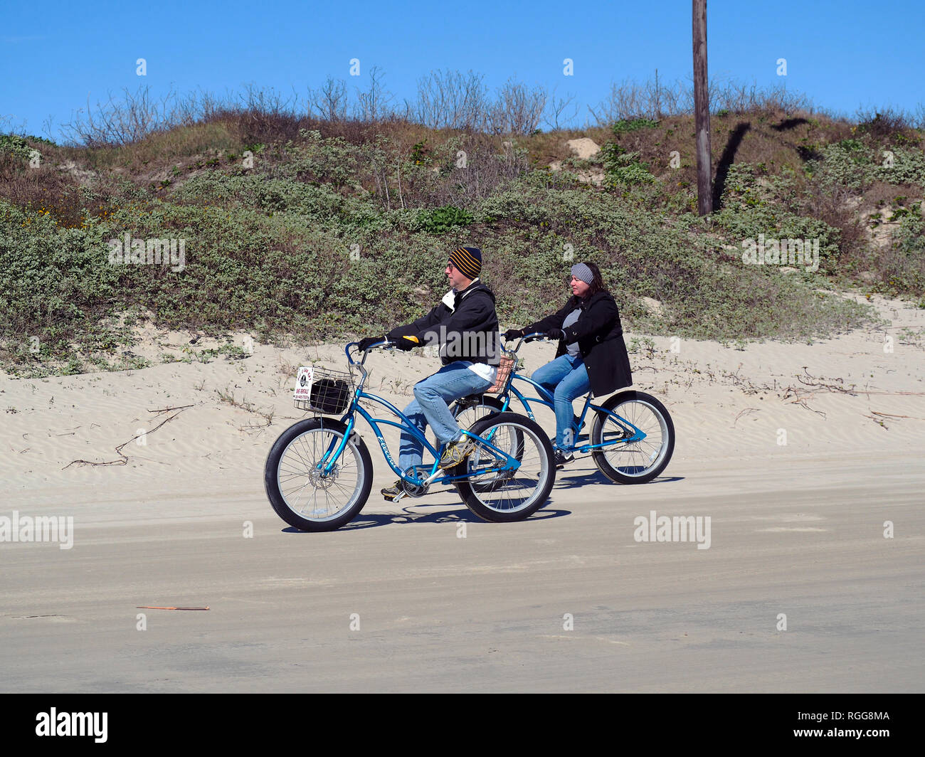 Un caldo vestito uomo e donna ride beach cruiser biciclette di stile al fresco gennaio meteo sulla spiaggia in Port Aransas, Texas, Stati Uniti d'America. Foto Stock