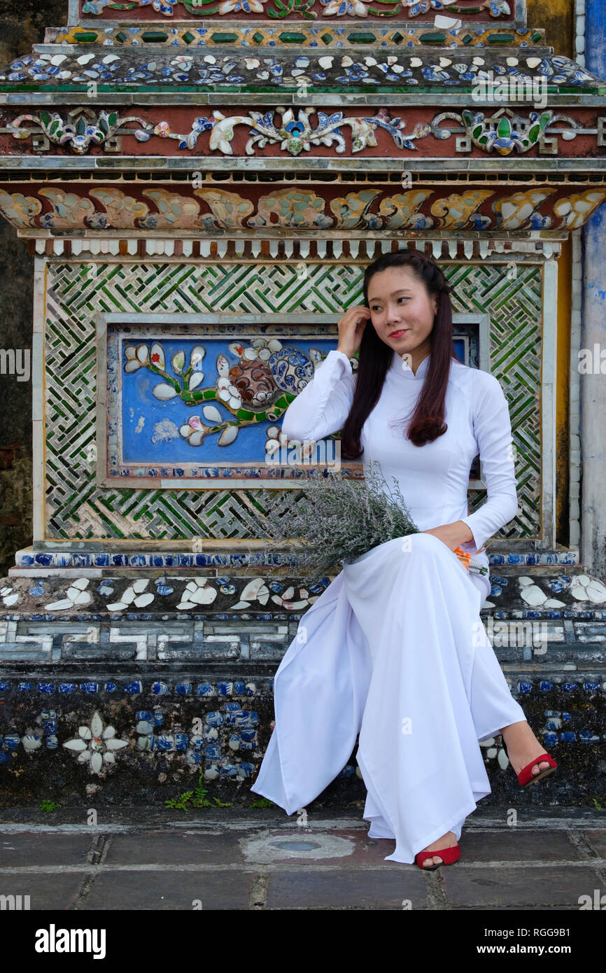 Ritratto di una giovane donna che indossa al tradizionale vietnamita indumento nazionale Áo dài mentre la visita della cittadella imperiale di Hue, Vietnam Asia Foto Stock