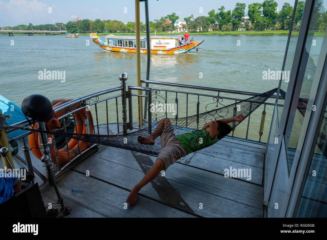 Kid poggiante su amaca a bordo di una barca turistica crociera sul Fiume Perfume, tonalità, Vietnam Asia Foto Stock