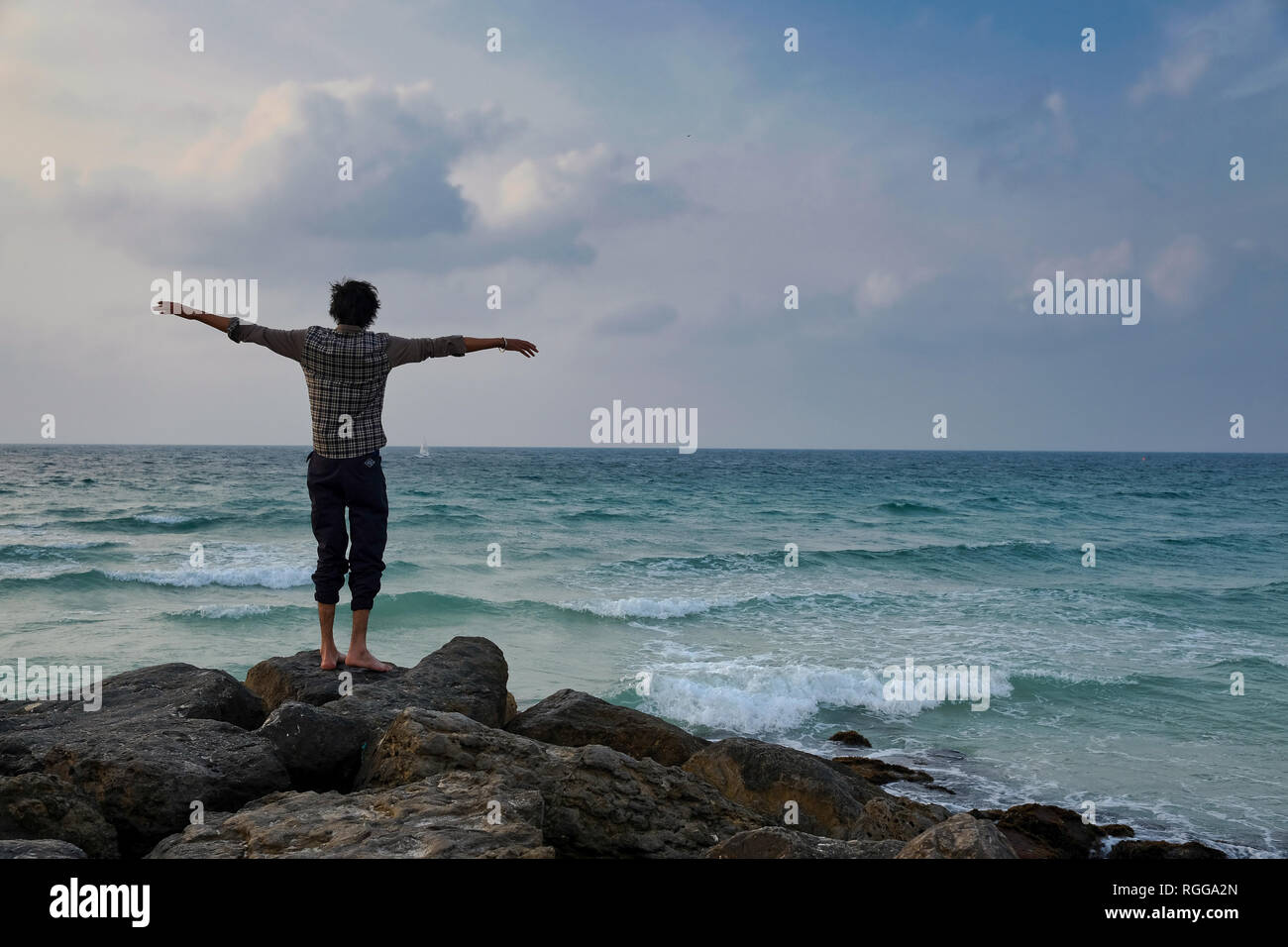 Un giovane adulto in piedi sulle rocce al ​beach con le braccia aperte ampia Foto Stock