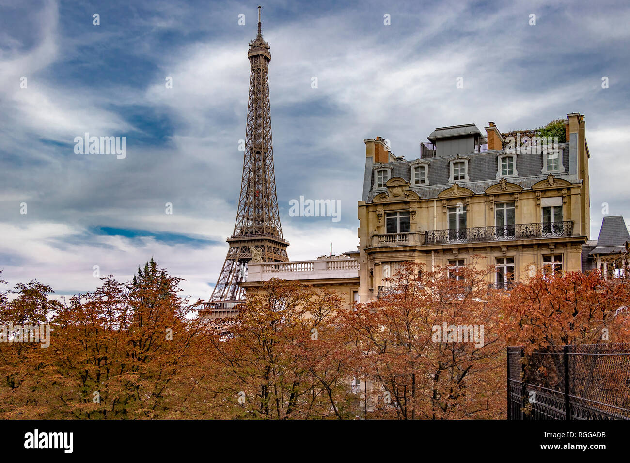 La Torre Eiffel si siede dietro un grande appartamento di Parigi edificio come visto da Avenue de Camoens con gli alberi girando un autunnale di colore arancione , Parigi Foto Stock