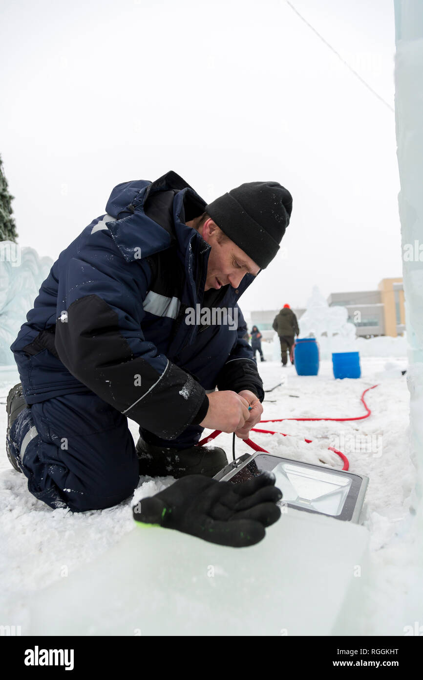 Elettricista pulisce le estremità del cavo di alimentazione per illuminare le figure di ghiaccio Foto Stock
