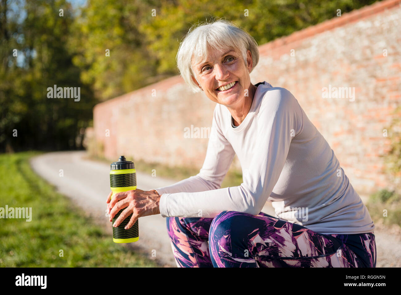 Sorridente sportive donna senior tenendo la bottiglia in posizione di parcheggio Foto Stock